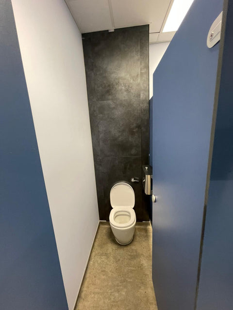 An Ascent Range toilet cubicle with a blue door, open onto a WC with dark IPS panelling behind it
