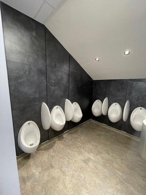 Dark stone-effect IPS panelling behind a row of urinals, under a sloping ceiling
