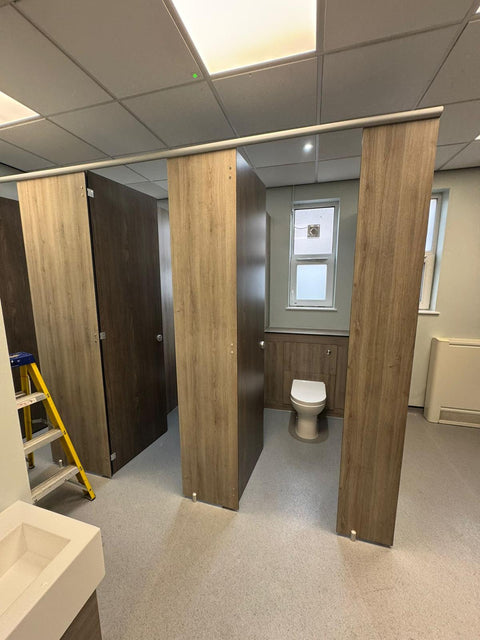 Half-height IPS in dark woodgrain behind a WC, inside a run of woodgrain Alpine Range cubicles during installation