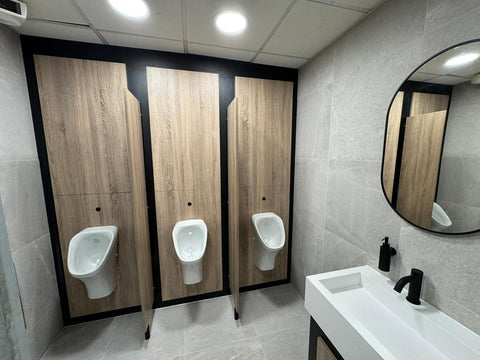 Woodgrain compact laminate IPS behind three urinals, with matching privacy screens and black edges