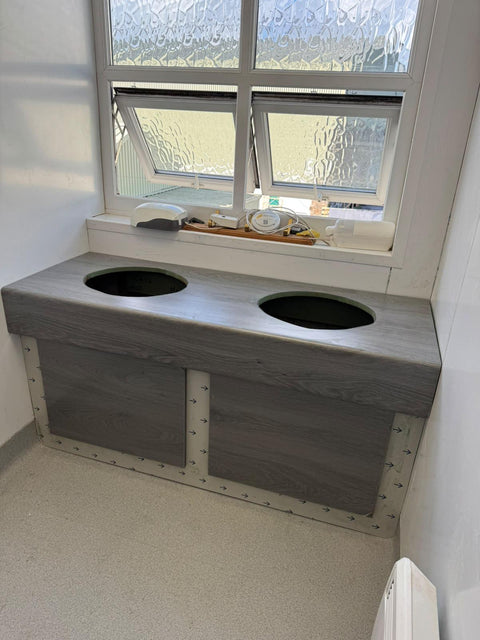 Two-basin vanity unit with a grey woodgrain top and access panels, during installation before the basins go in