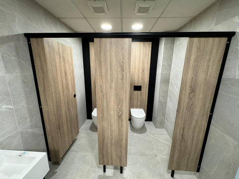 Ascent Range toilet cubicles with woodgrain doors and a black headrail, fitted in front of matching IPS panelling