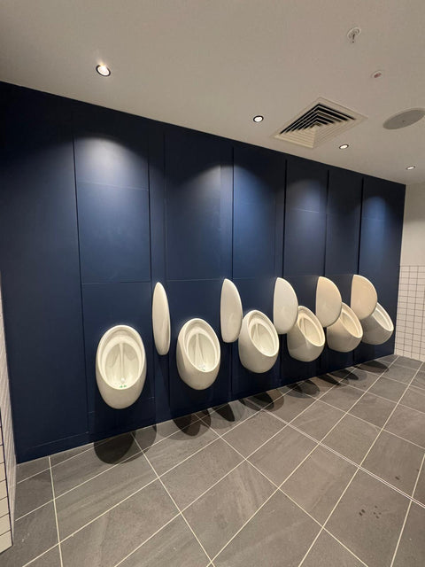 Navy blue IPS panelling behind a row of urinals with privacy screens, in a commercial washroom