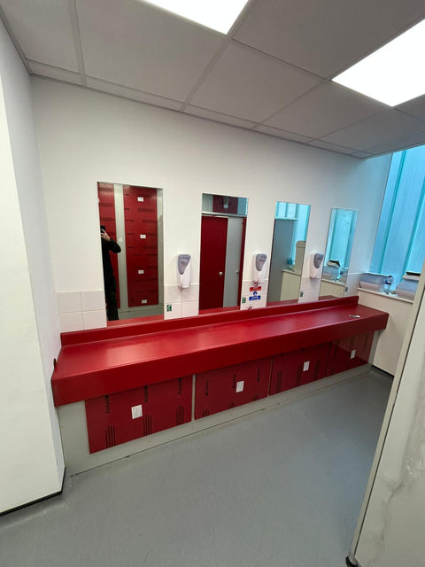 Red vanity unit with a long integrated trough and vented red access panels, in a commercial washroom