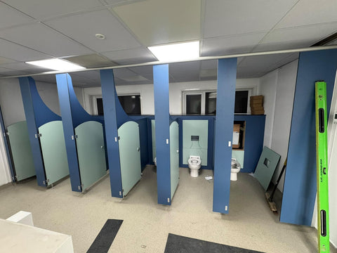 Half-height IPS with mint-green access panels behind the WCs, in a run of Blossom Range nursery cubicles during installation