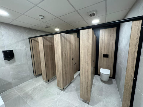 Smart Range toilet cubicles with woodgrain doors and a black headrail, installed in a tiled commercial washroom