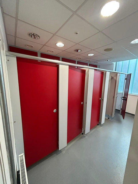 A row of Smart Range toilet cubicles with red doors and white pilasters, installed in front of matching panelling