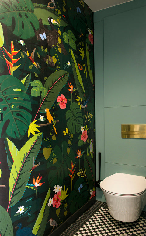 Sage green IPS panelling behind a wall-hung WC with a brass flush plate, beside a tropical feature wall